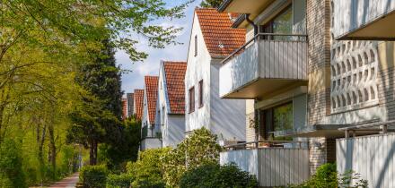 Modern german street with white stoned houses with tiled roofs. Sunny day and green alley.