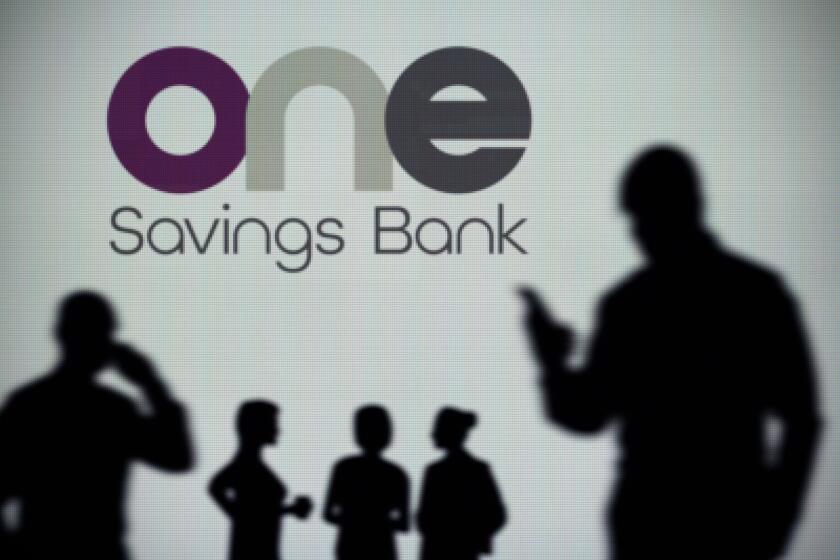 The OneSavings Bank logo is seen on an LED screen in the background while a silhouetted person uses a smartphone (Editorial use only)