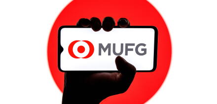 Smartphone with Mitsubishi UFJ Financial Group logo on screen in clenched hand on background of Japan flag