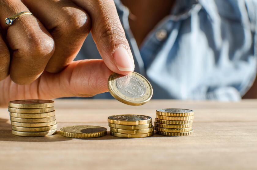 Closeup of a black woman hand counting Euro coins on a wooden table. Selective focus,