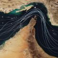 Satellite view of the Strait of Hormuz with white graphic lines representing global shipping lanes and maritime traffic between the Persian Gulf and G