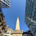Looking up at The Monument against a vivid blue sky surrounded by office buildings in City of London