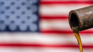 A close up of a piece of metal pipe from which oil is pouring, against the backdrop of an American flag. Mineral oil on factory on background of unite