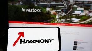 Person holding smartphone with logo of company Harmony Gold Mining Co. Ltd. on screen in front of website. Focus on phone display.