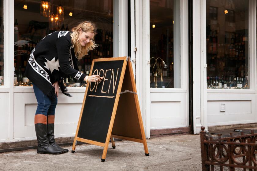 female small business owner making open sign outside wine shop
