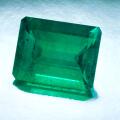 A large natural emerald cut emerald sits on a silver reflective background.