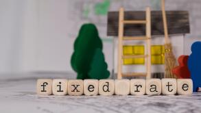 Words FIXED RATE composed of wooden letters. composed of wooden letter. Small paper house, wooden trees in the background. Closeup
