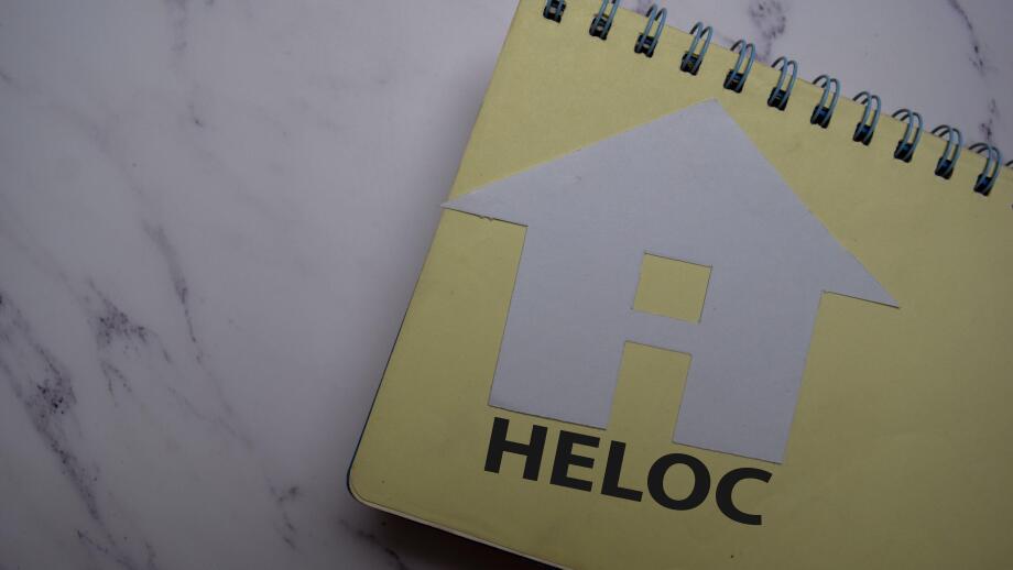 HELOC write on sticky note and house made from paper isolated on Office Desk.