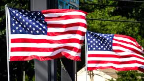 Two American flags wave vociferously in the wind in a suburban area