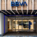 The BBVA bank branch in Cartagena, Spain, featuring a concrete ribbed facade, blue logo, and glass sliding doors illuminated by purple neon lights.