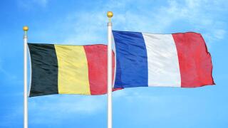 Belgium and France two flags on flagpoles and blue cloudy sky