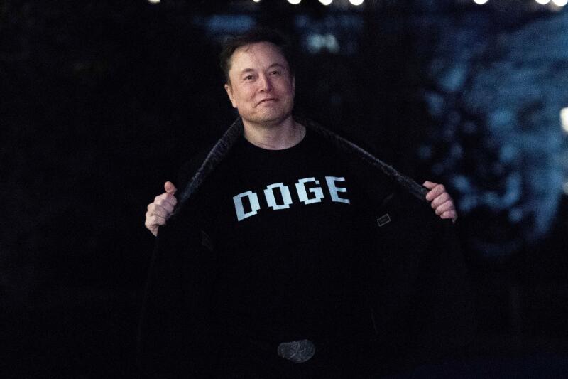 Elon Musk flashes his t-shirt that reads "DOGE" to the media as he walks on South Lawn of the White House, in Washington, Sunday, March 9, 2025. (AP Photo/Jose Luis Magana)