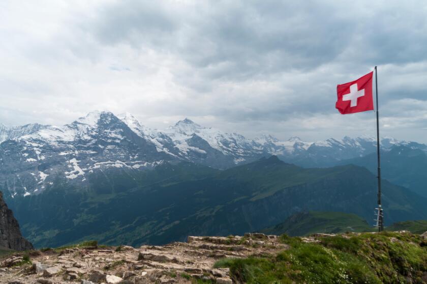 Swiss flag flown in strong wind. Bad weather, dark clouds, rain. In the background Eiger, Monch, and Jungfrau mountains.