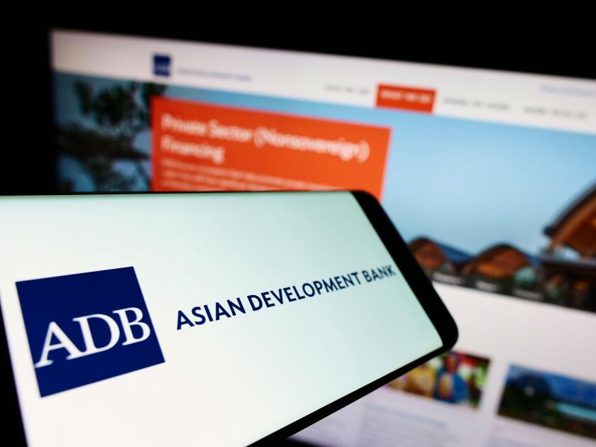 Smartphone with logo of organization Asian Development Bank (ADB) on screen in front of business website. Focus on center-left of phone display.