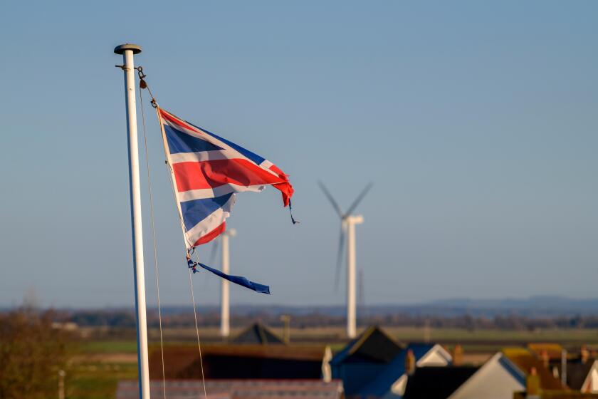 A tattered Union Jack flag fluttering in the wind against a blue sky.