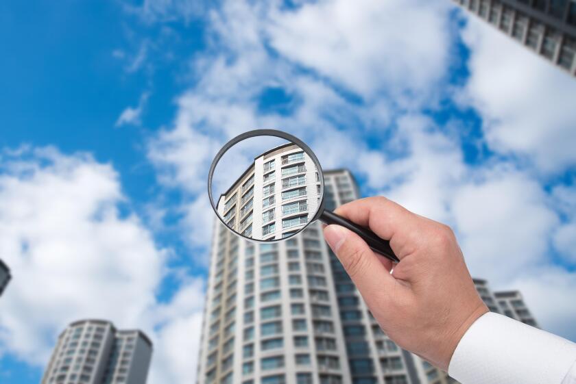 A hand holding a magnifying glass against the backdrop of an apartment.