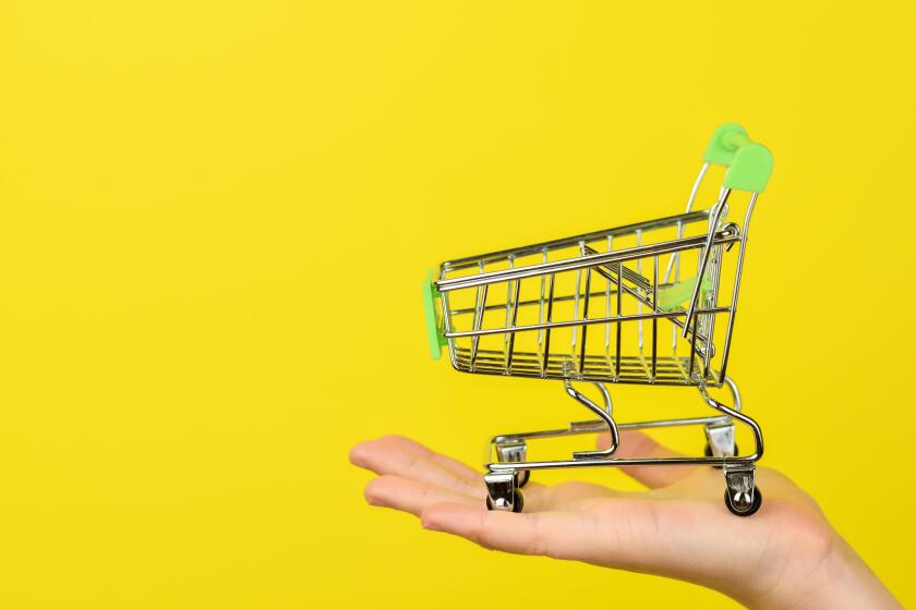 Empty shopping cart on female hand. Shopping theme. Small Trolley isolated on a bright yellow background. Consumer concept, Copy space.