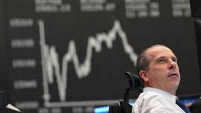 25 January 2022, Hessen, Frankfurt/Main: Securities trader Arthur Brunner from ICF Bank looks at his monitors at his workplace on the floor of the Frankfurt Stock Exchange in front of the display board showing the Dax curve. After the price plunge at the 