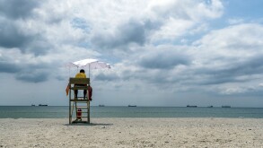 A lifeguard sitting on surveillance tower, front of the sea. Lifeguard Beach Chair. Beach lifeguard on duty. Cloudy sky.