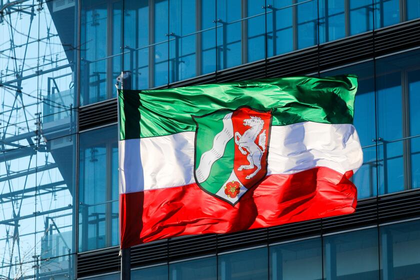 NRW North Rhine-Westphalia flag on flagpole blowing in the wind in front of the facade of the city gate, Dusseldorf, North Rhine-Westphalia, Germany